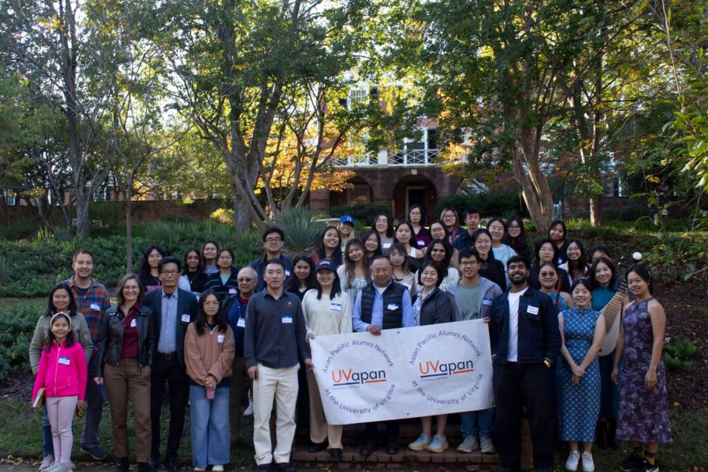 Group photo of garden party attendees holding the APAN banner. There are about 40 or 50 people in the photo.