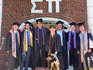 Group of actives in graduation regalia, along with a dog